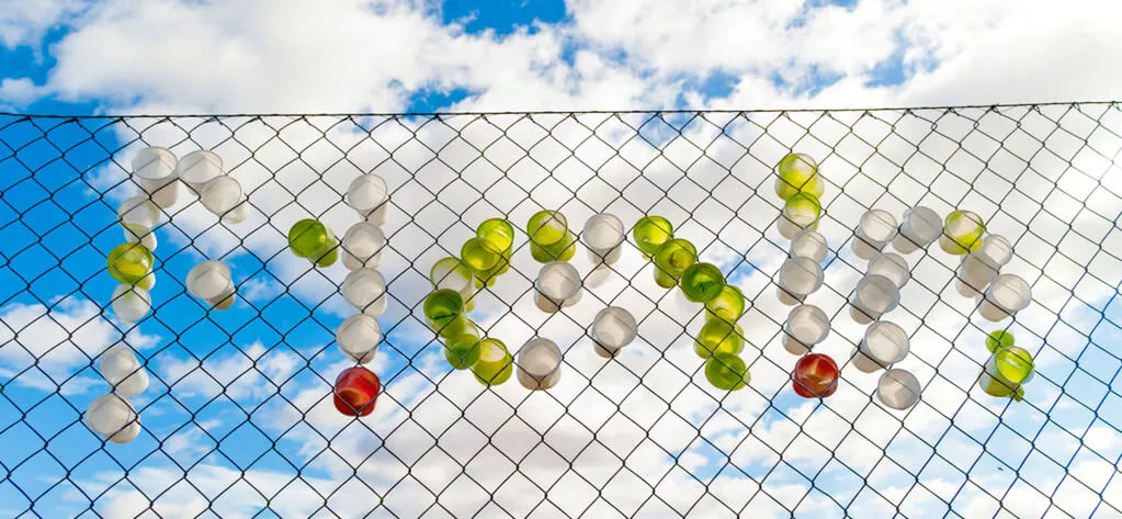 Colored cups arranged in a chain-link fence beneath a blue sky with white clouds.